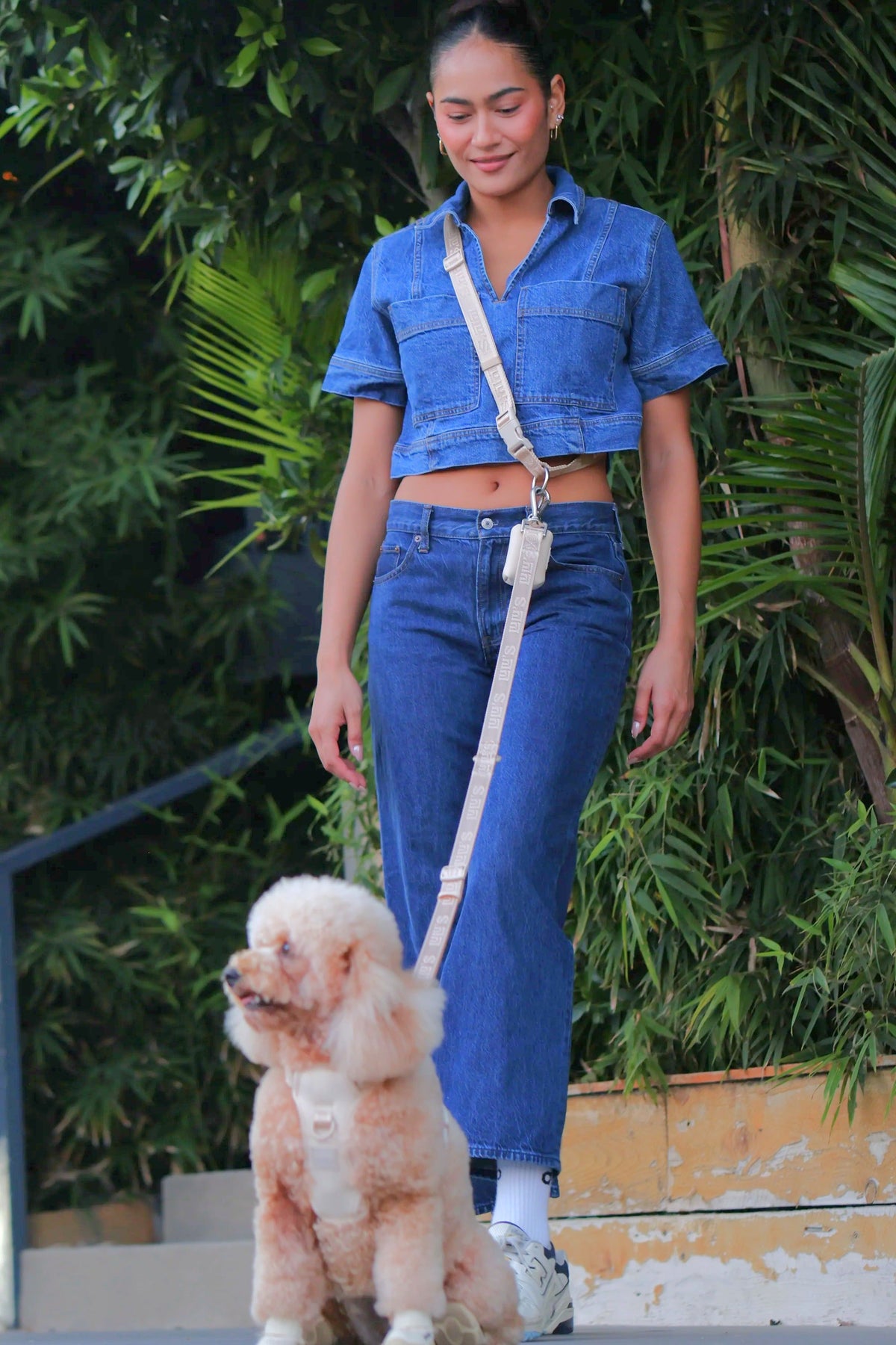 Woman wearing an Oat Beige Lulu's from Cali hands-free walking belt crossbody, walking a poodle