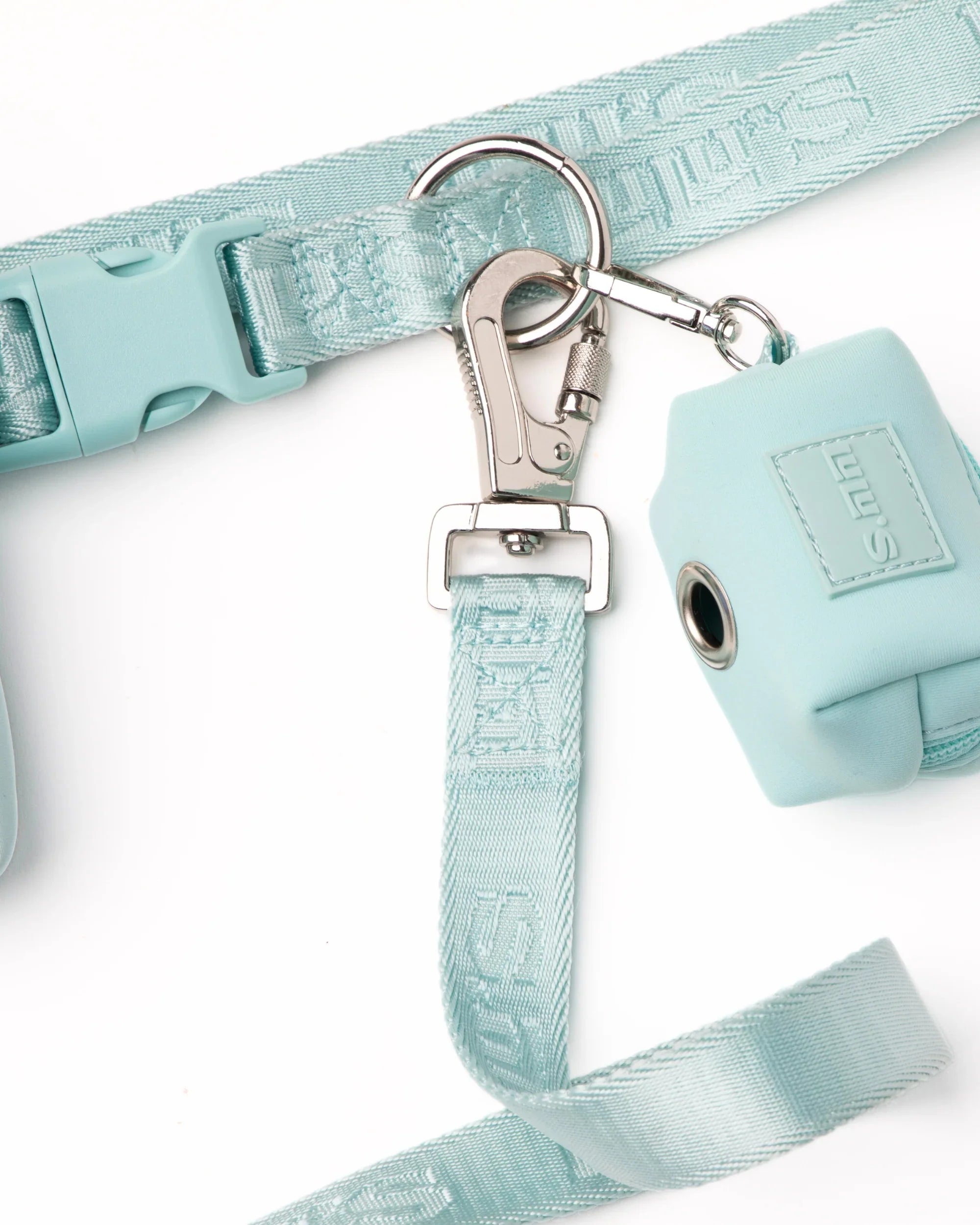 Close-up of a light blue dog leash clipped to a metal hook, with an attached matching waste bag pouch featuring the embossed “LULU’S” logo, all resting on a white background.
