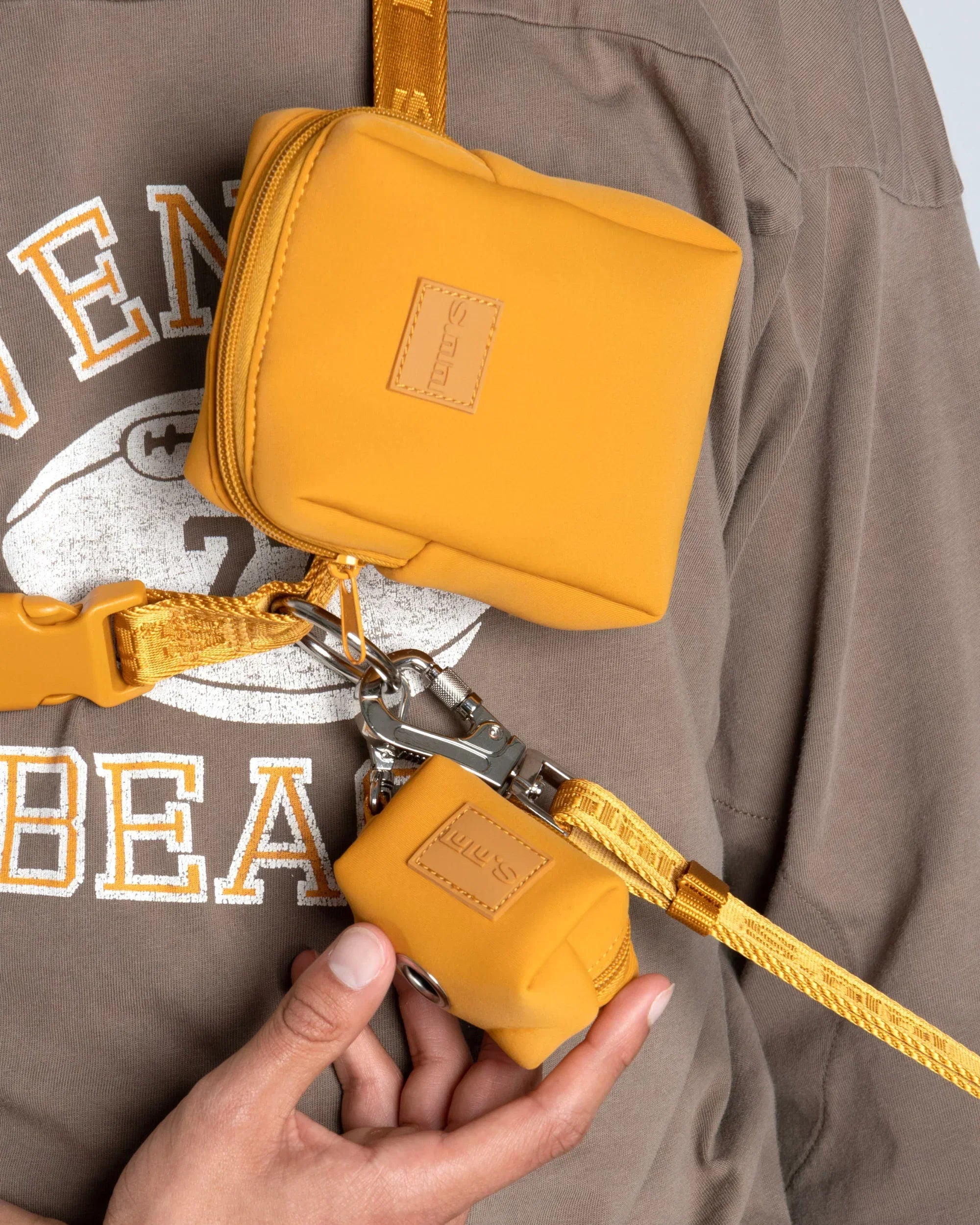 Sunburnt orange dog waste bag pouch and leash clipped to a matching belt, worn crossbody over a brown sweatshirt.