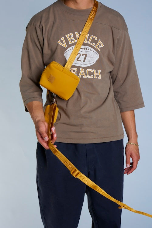 A person wearing a brown 'Venice Beach' t-shirt and dark pants, carrying a Sunburnt Orange waist bag and holding a matching Sunburnt Orange leash